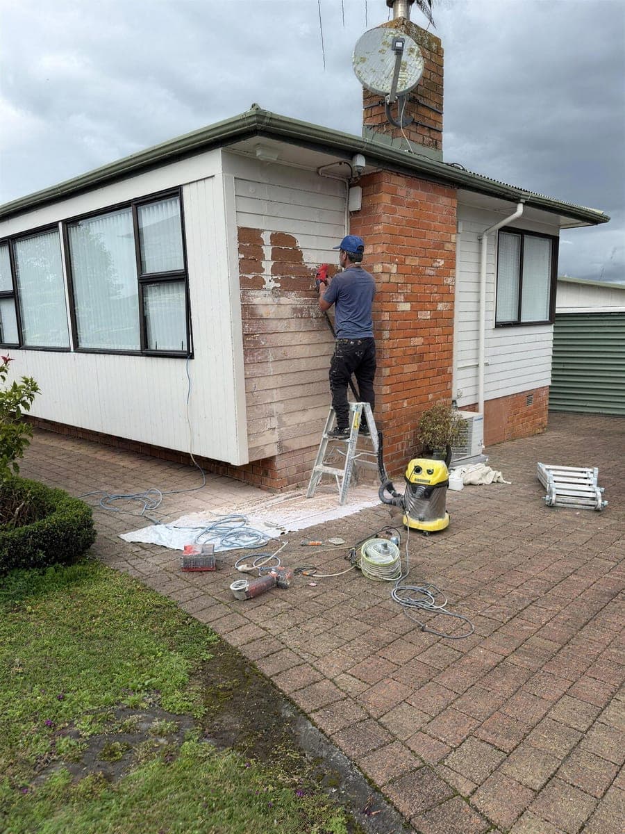 EGP painter on a ladder stripping failed paint from exterior brickwork